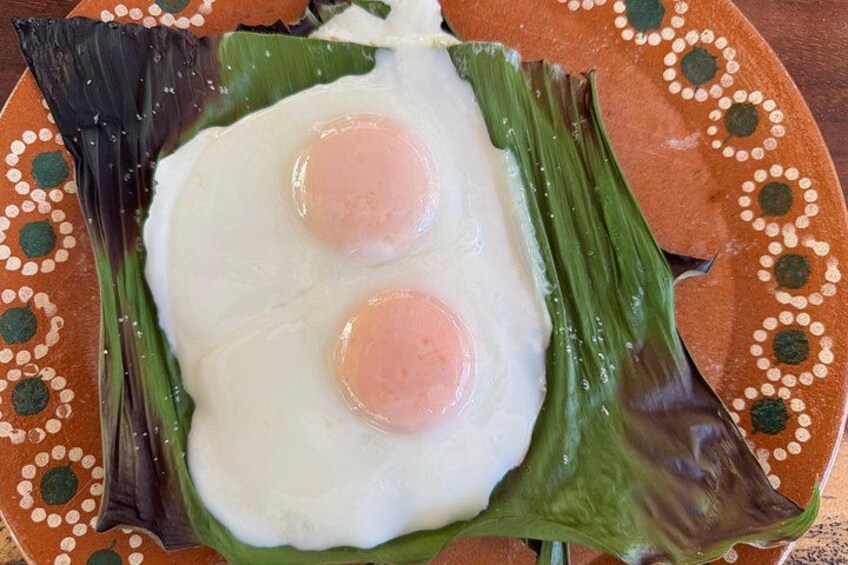 Un plato con dos huevos fritos sobre una hoja de plátano. 4
