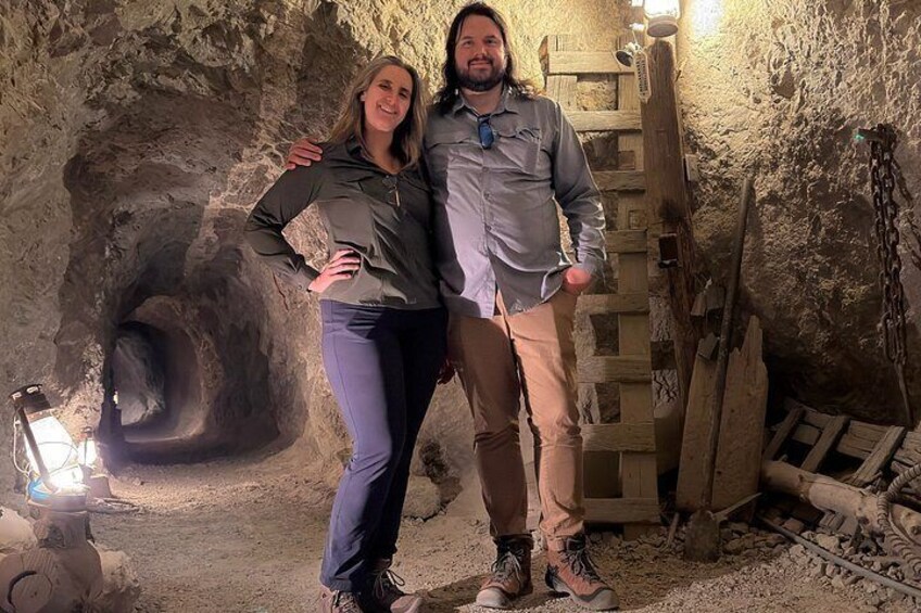 Zwei Personen stehen in einer Höhle mit einer Holzleiter und einer Lichtquelle. 5