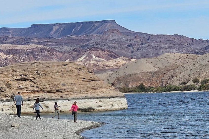 A group of people walking along a riverbank with a mountainous landscape in the background. 5