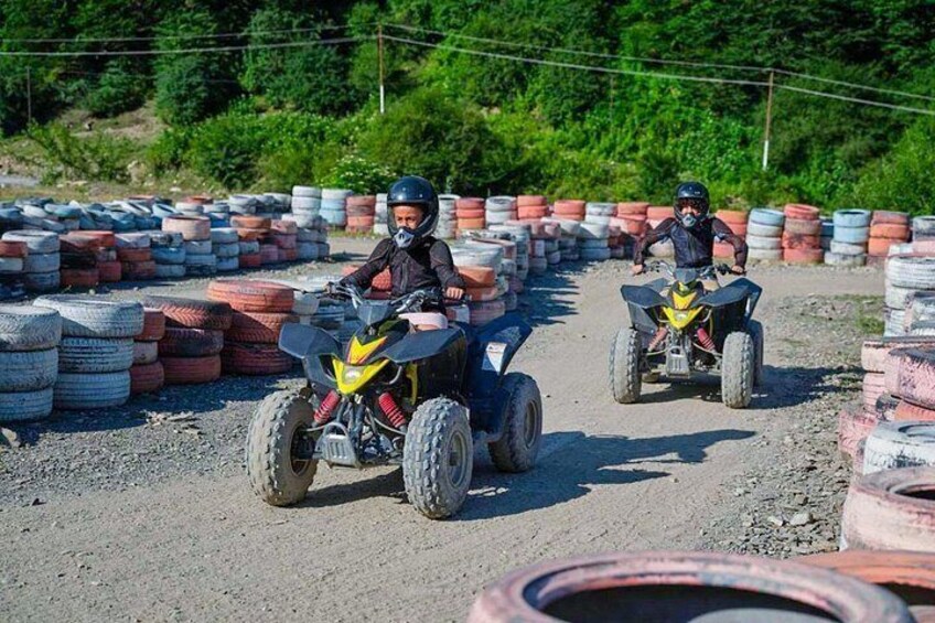 Two people riding ATVs on a dirt track surrounded by stacks of tires. 4