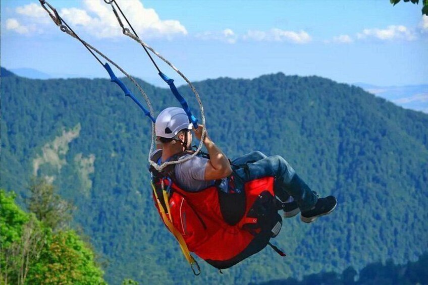 A person on a red suspension bridge with blue cables, surrounded by a mountainous landscape. 3