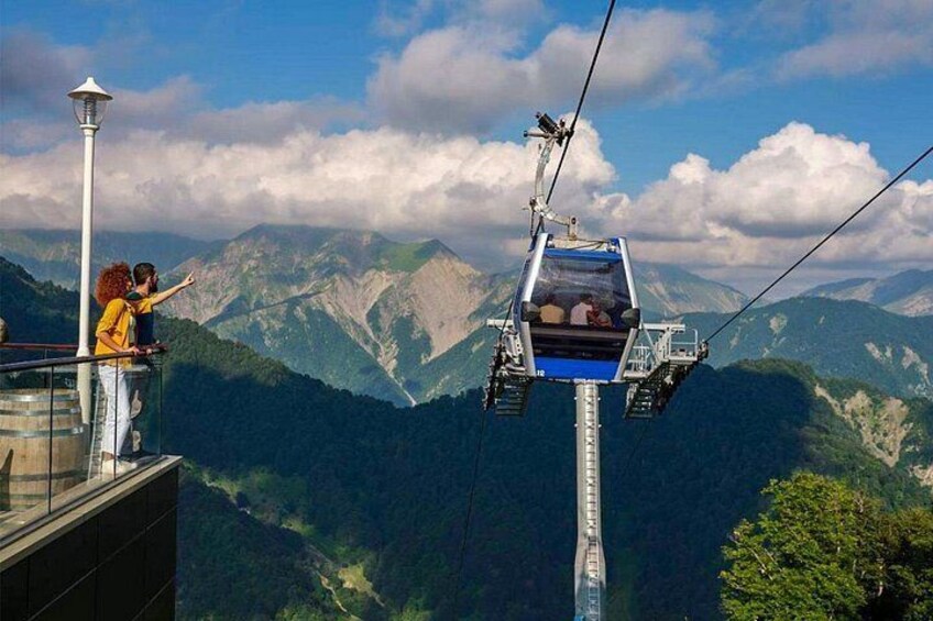 A cable car with passengers, a mountain landscape, and a person pointing at the view. 1