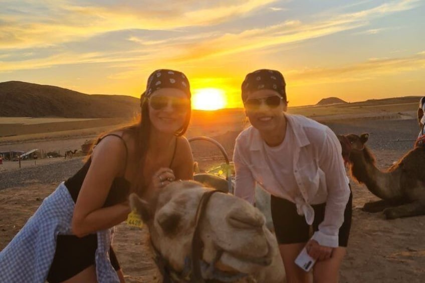 Two people interacting with a camel in a desert landscape during sunset. 4