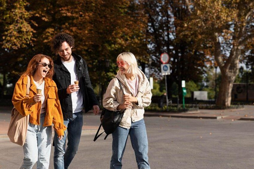 Three people walking on a street, holding drinks, with autumn trees and a road sign in the background. 2