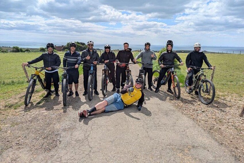 A group of cyclists on a dirt path with a grassy field and a cloudy sky in the background. 3