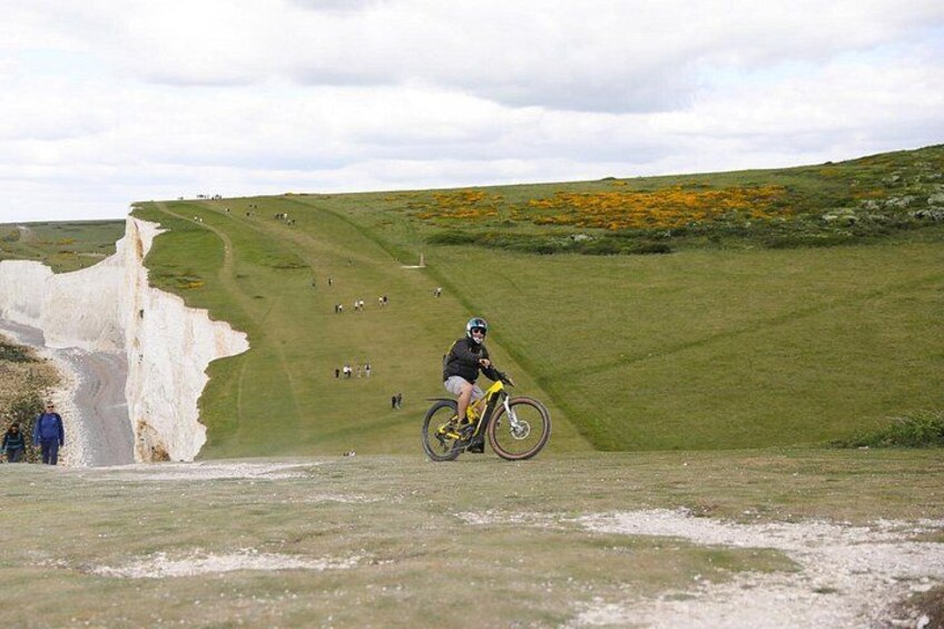 A cyclist on a dirt path with a white cliff and green fields in the background. 4