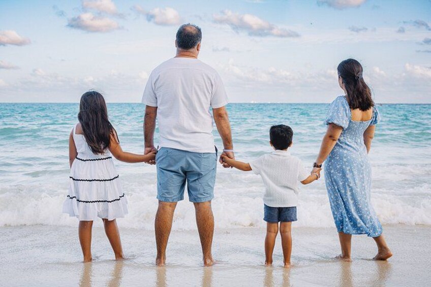 En familie på fire holder i hånd på en strand med havet i baggrunden. 5