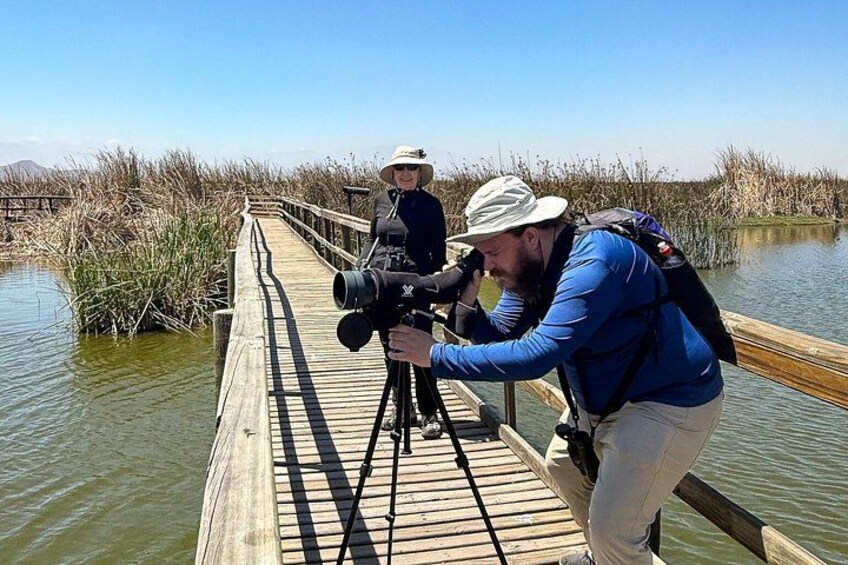 A wooden boardwalk over water with people using a camera on a tripod. 1