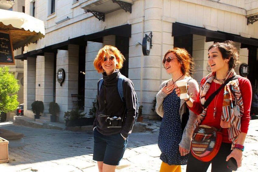 Three people walking on a cobblestone street, a building with a signboard, and a tree. 5