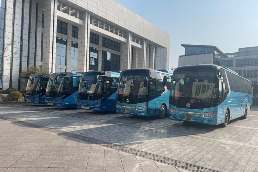 A row of blue buses parked in front of a modern building with large windows. 2