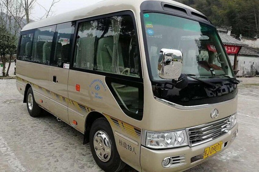 A beige bus with a front license plate, side mirrors, and a logo on the side. 3