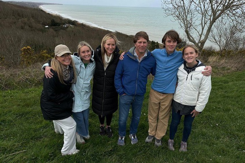 Een groep mensen staat op een grasheuvel, met uitzicht op de zee en heuvels op de achtergrond. 5