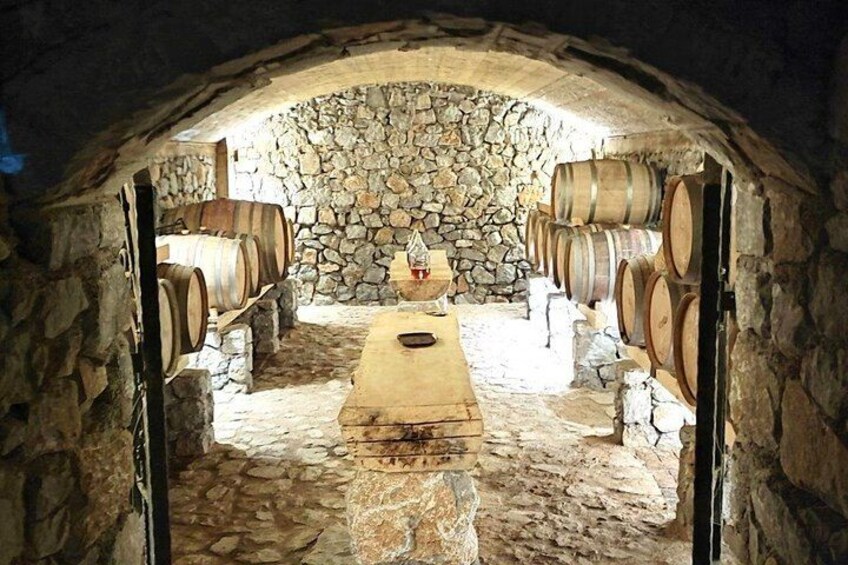 A cellar with stone walls, wooden barrels, and a central table. 3