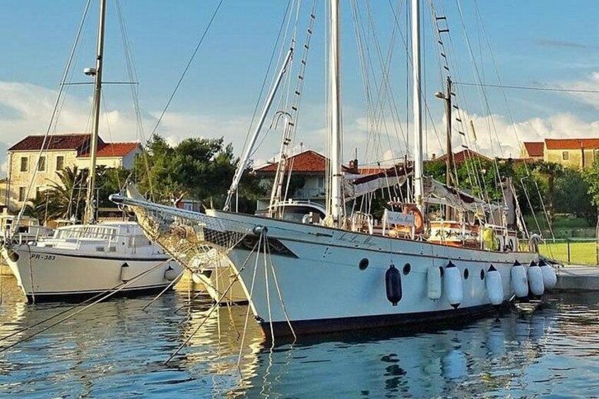 A large white sailing boat docked at a marina with other boats, surrounded by buildings and greenery. 4