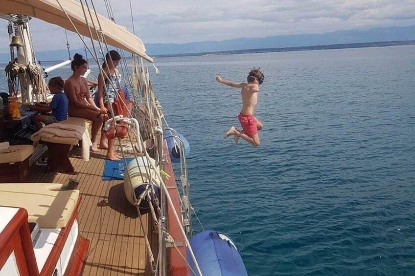 A person jumping from a boat into the water, with other people on the boat and a calm sea in the background. 1