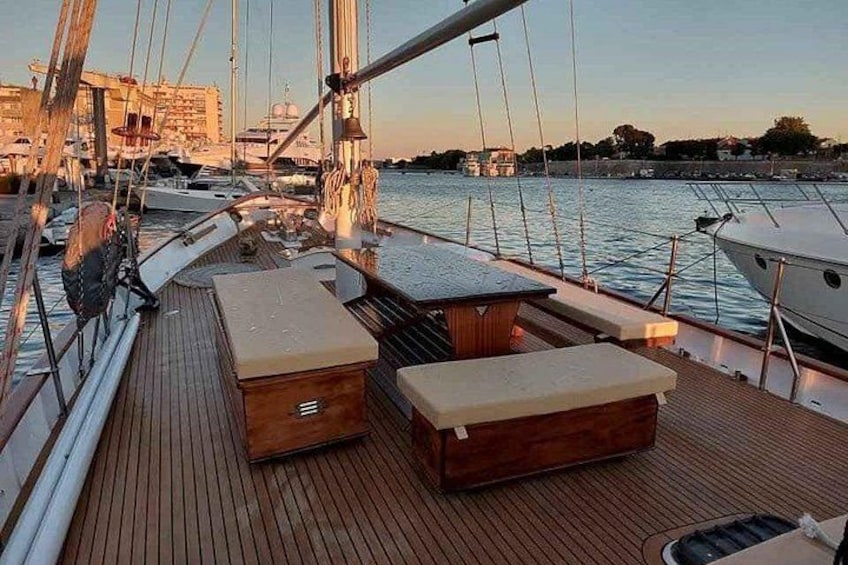 A wooden deck with seating, a sailboat, and a marina in the background. 3