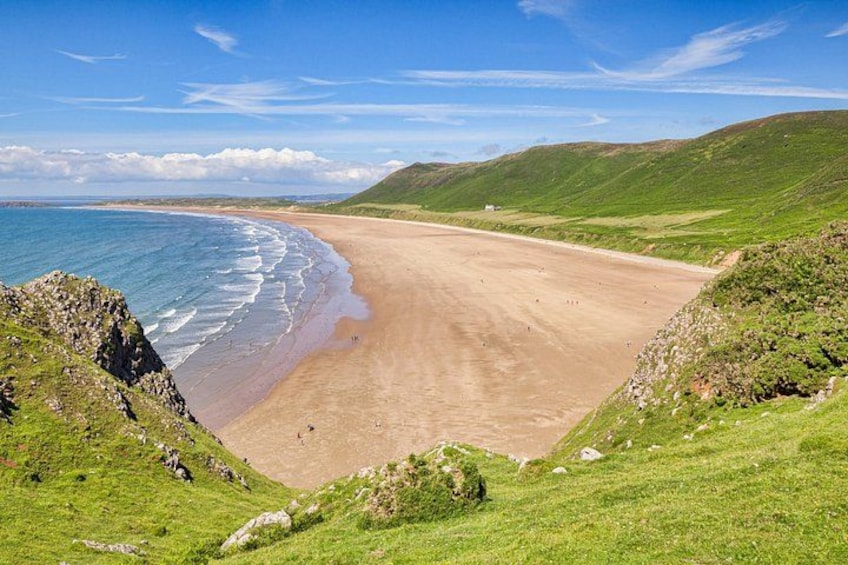 A coastal landscape with a sandy beach, grassy hills, and a clear blue sky. 1