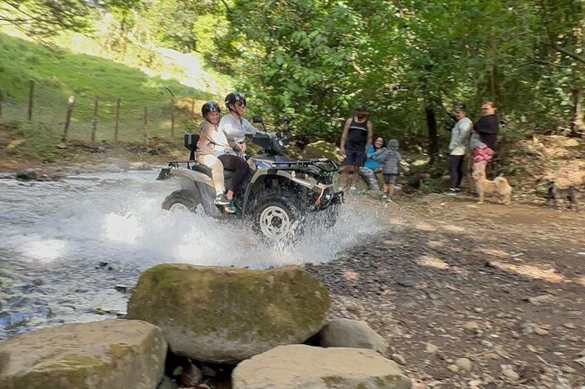 Un cuatrimoto cruzando un arroyo poco profundo, rodeado de rocas y follaje. 5