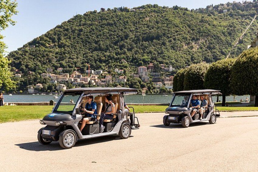 Two golf carts on a paved road with a lake and a hill in the background. 4