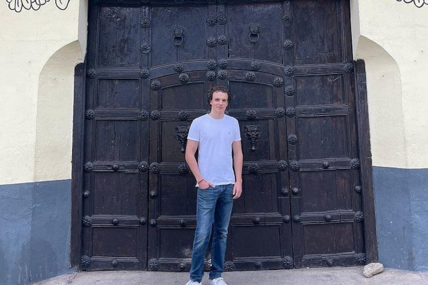 A person standing in front of a large, ornate wooden door with a decorative handle. 3