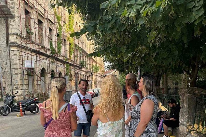 A group of people standing on a street with historical buildings and trees. 3