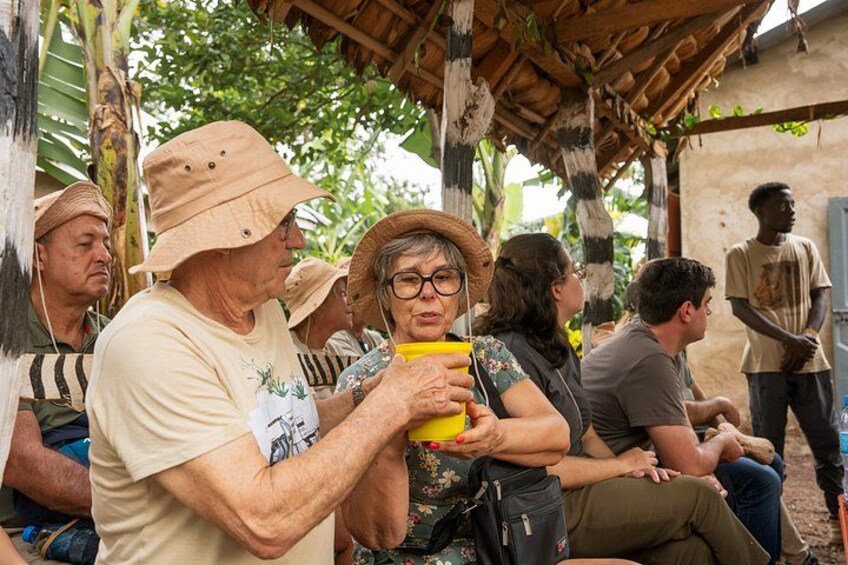 A group of people sitting under a thatched roof structure, some holding yellow objects. 3