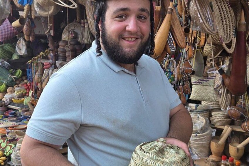 A person holding a woven basket in a market with various handmade items and baskets in the background. 4