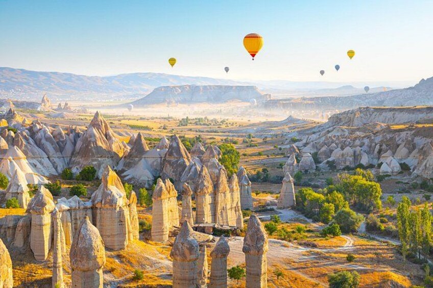 A landscape with distinctive rock formations, a clear sky, and hot air balloons. 1