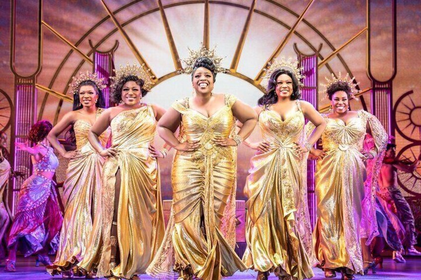 A group of people in golden dresses on a stage with a circular backdrop. 2