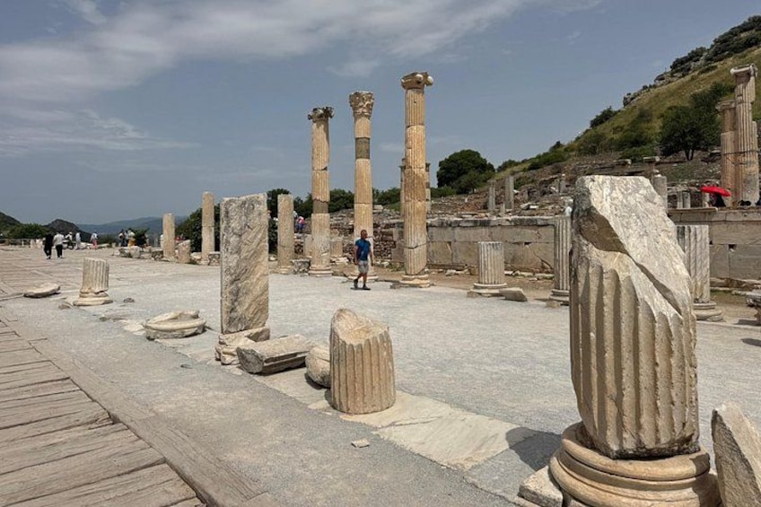 Ancient ruins with columns and stone blocks, a wooden walkway, and a hilly background. 4