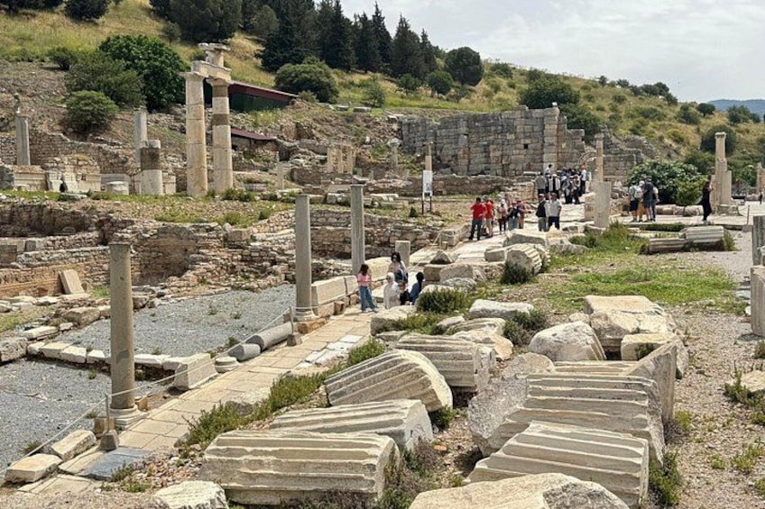 Ancient ruins with stone columns and steps, surrounded by greenery and a few visitors. 3