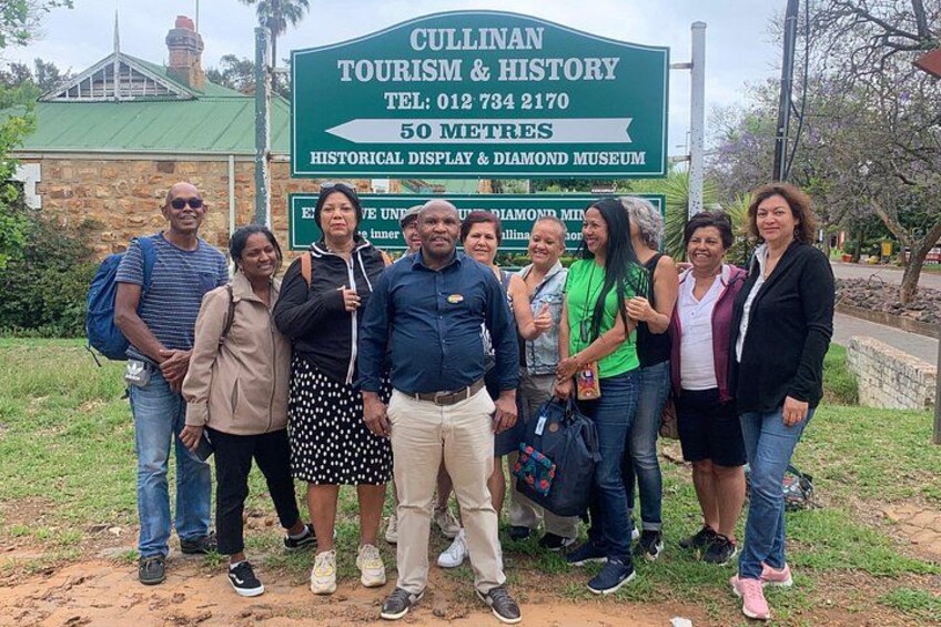 Un grupo de personas frente a un cartel de Cullinan Tourism & History. 1