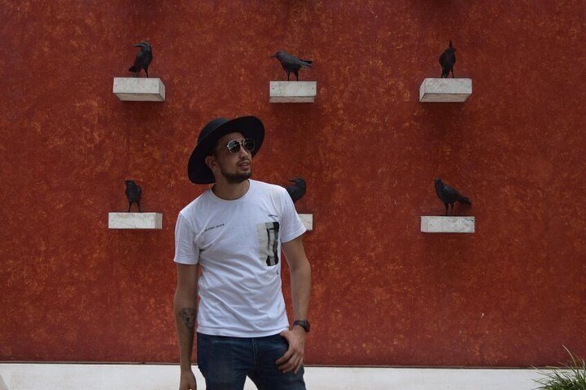 A person standing in front of a red wall with bird sculptures. 4