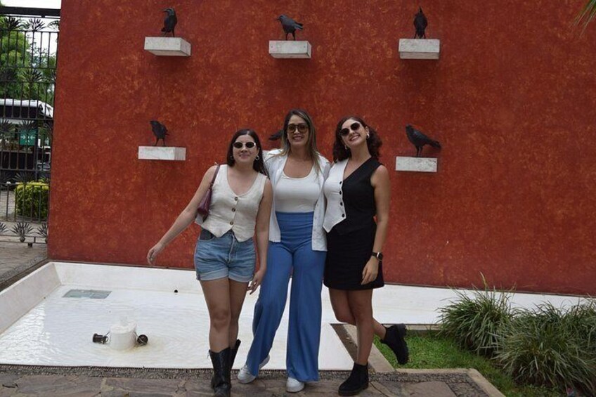 Three people standing in front of a red wall with bird sculptures. 2