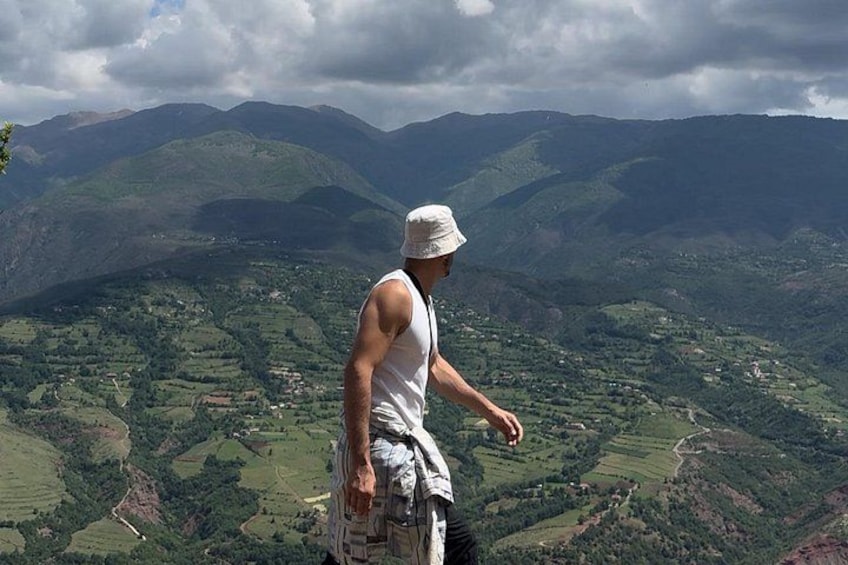 A person standing on a mountain overlooking a valley with green fields and distant hills. 1