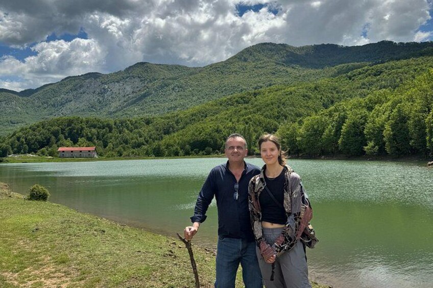 A lake with mountains in the background, a red building on the shore, and a person holding a walking stick. 4