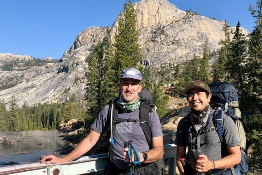 Two people with backpacks standing by a boat in a mountainous area with a lake. 2
