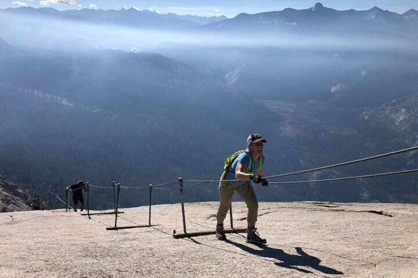 A person on a mountain trail with a rope barrier, wearing a backpack and hiking boots. 4