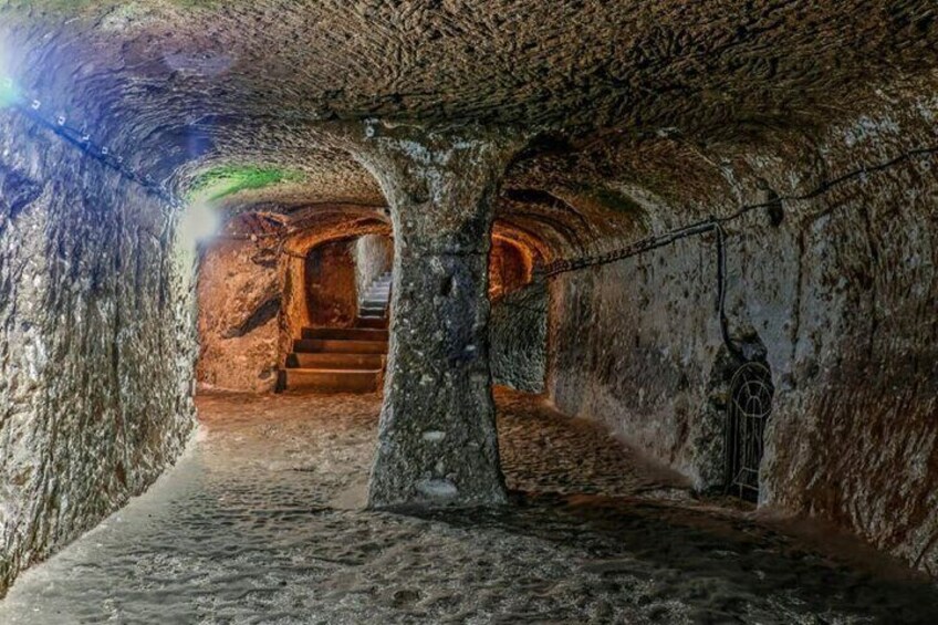 Un túnel subterráneo con paredes de piedra, una escalera y una cadena colgante. 4