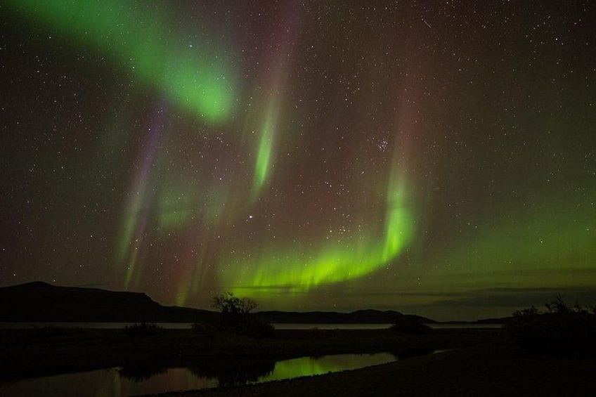 The Northern Lights over a landscape with a body of water and hills. 2