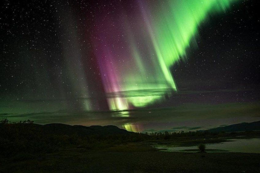 The Northern Lights over a landscape with a body of water and hills. 3