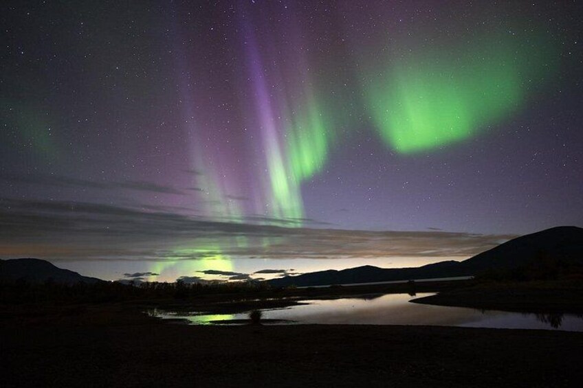 Nattehimmel med nordlys over en rolig sø, med bjerge i baggrunden. 1
