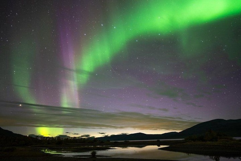 A night sky with aurora borealis over a calm lake and distant mountains. 4