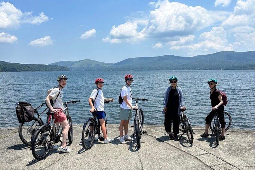 A group of cyclists on a lakeside path with mountains in the background. 4