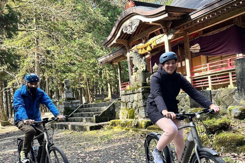 Two people on bicycles in front of a traditional Japanese building with a stone staircase. 3