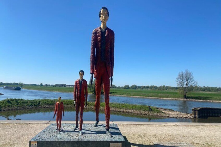 En skulptur af tre figurer i rødt på en platform ved en flod. 1