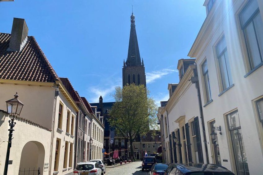 En gade med bygninger, et kirketårn og parkerede biler. 3