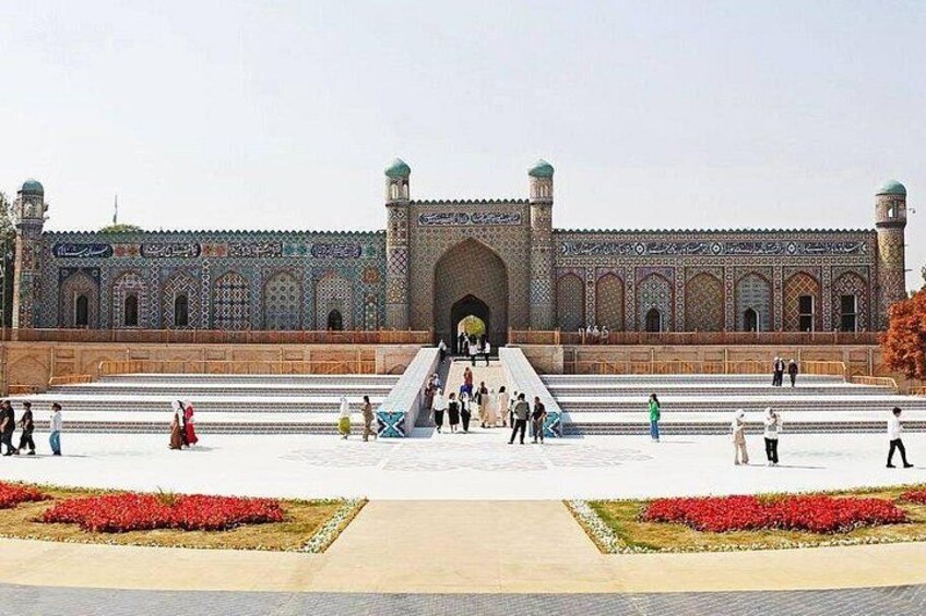 A large, ornate building with a grand entrance, surrounded by a spacious courtyard with red flower beds and a central staircase leading up to the entrance. 5
