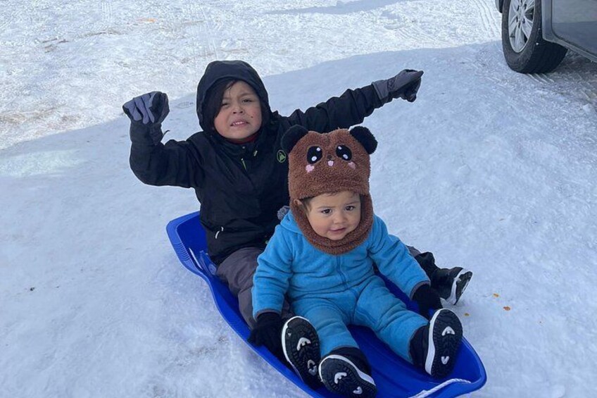 Two children sledding on a snowy surface. 2