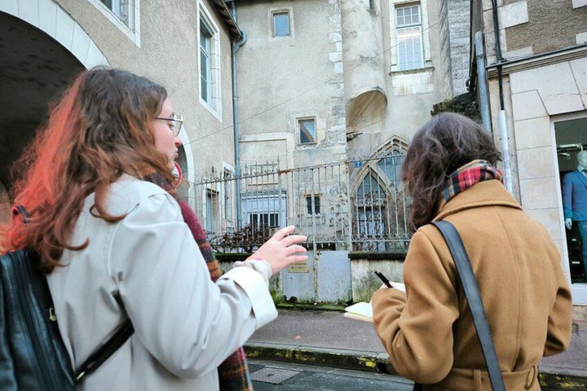 Zwei Personen gehen auf einer Straße, im Hintergrund sind Gebäude und ein Zaun zu sehen. 3